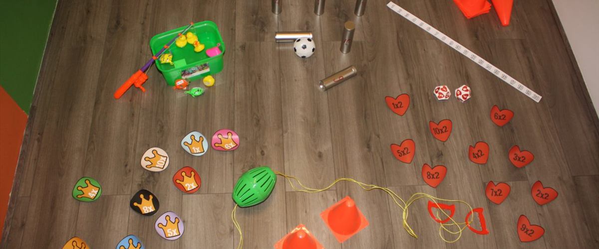 Materiaal voor de bootcamp op de vloer: tafelsommen op kaarten, genummerde blikken, pionnen, een bal en een meetlint