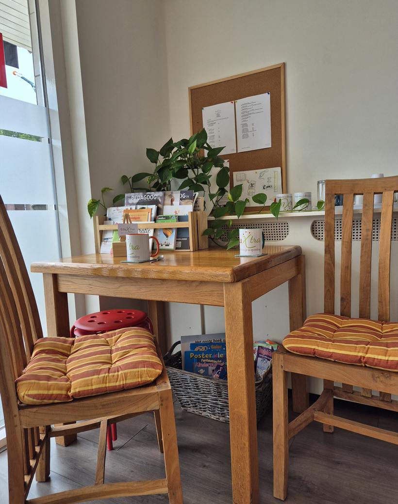 De ontvangstruimte bij EduXtra: een houten tafel met twee stoelen, folders en EduXtra-mokken